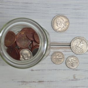Top view of a jar filled with coins placed on a wooden table, depicting savings.